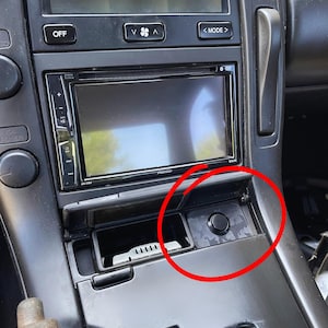 Puede incluir: Panel de instrumentos de coche negro con un sistema estéreo Pioneer, controles de aire acondicionado y un pequeño compartimento de almacenamiento. El salpicadero es de color gris oscuro con un acabado mate. Se ve un botón negro redondo.