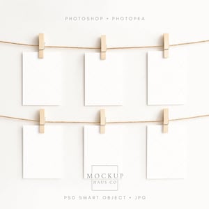 Puede incluir: Seis tarjetas blancas en blanco están sujetas a dos cuerdas con pinzas de madera sobre un fondo blanco. Las palabras "PHOTOSHOP • PHOTOPEA" están en la parte superior, y "MOCKUP HAUS CO" y "PSD SMART OBJECT • JPG" están en la parte inferior.