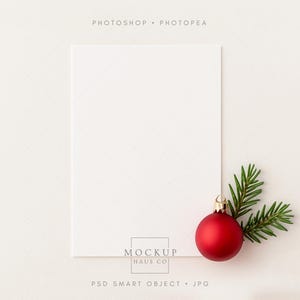 May include: A blank white card with a textured surface, a red Christmas ornament, and a sprig of green pine needles. The ornament has a gold cap. The text "PHOTOSHOP • PHOTOPEA" is at the top. The text "MOCKUP HAUS CO" is at the bottom.