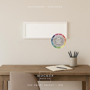 Pode incluir: Uma moldura retangular branca está pendurada acima de uma mesa de madeira. Um gráfico de roda de cores com o texto "ONE MOCKUP, MANY LOOKS!" está ao lado da moldura. Um bloco de notas, um lápis e lápis em um suporte cinza estão na mesa. O texto "MOCKUP HAUS CO" é visível.
