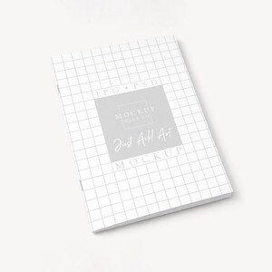 May include: A white notebook with a grid pattern and the text "Just Add Art Mockup" in a gray square. The notebook is on a white surface.