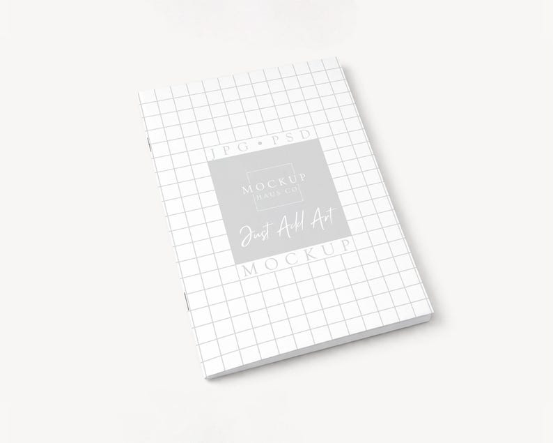 May include: A white notebook with a grid pattern and the text "Just Add Art Mockup" in a gray square. The notebook is on a white surface.