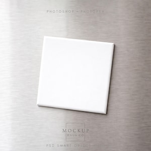 Puede incluir: Un lienzo cuadrado blanco sobre una superficie de metal cepillado. El lienzo está centrado y parece estar en blanco, con una estética limpia y minimalista. El fondo es de color gris plateado texturizado.