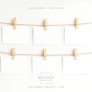May include: Six blank white cards are clipped to two strands of twine with wooden clothespins. The cards are arranged in two rows of three against a white background. The words "PHOTOSHOP • PHOTOPAE" are at the top. The words "MOCKUP HAUS CO" are at the bottom.