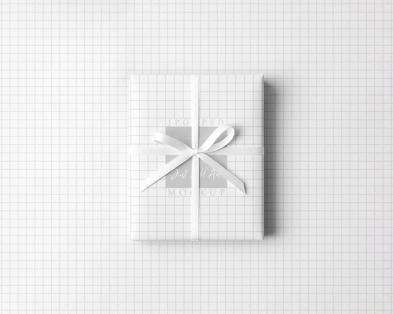 May include: A wrapped gift with white grid paper and a white satin ribbon tied in a bow. The gift is centered on a white grid background. The text "JPG PSD MOCKUP" is visible on the gift.