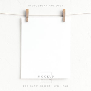 May include: A blank white square paper is suspended by two wooden clothespins on a thin string. The words "PHOTOSHOP • PHOTPEA" are above the paper. Below the paper is the text "MOCKUP HAUS CO" and "PSD SMART OBJECT • JPG • PNG".