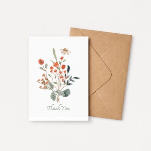 May include: A white greeting card with a watercolor floral design featuring orange and green foliage. The card reads "Thank You" in a script font. A brown envelope is next to the card.