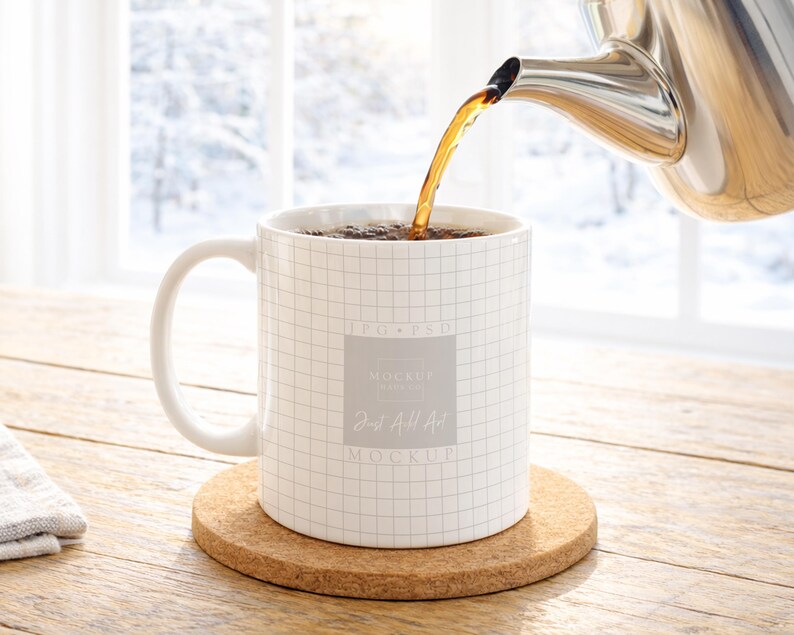 May include: A white ceramic mug with a grid pattern is being filled with tea from a stainless steel teapot. The mug sits on a round cork coaster. The text "Just All Art Mockup" is visible on the mug.