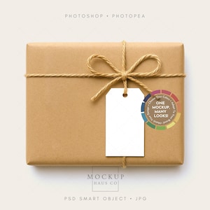 Könnte beinhalten: Ein rechteckiges Paket, das in braunes Papier gewickelt, mit Bindfaden verschnürt und mit einer Bindfaden-Schleife verziert ist. Ein leeres weißes Etikett hängt an der Schleife. Das Paket hat einen Farbkreis-Aufkleber mit dem Text "ONE MOCKUP, MANY LOOKS!"