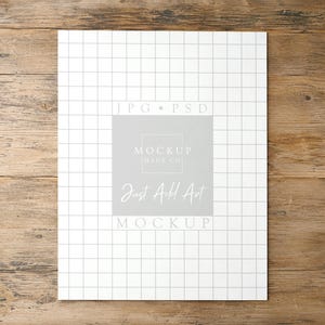 May include: A rectangular white paper sheet featuring a thin black grid pattern. Centered on the sheet is a light gray square containing the text JPG PSD, MOCKUP HAUS CO, Just Add Art, and MOCKUP in white and light gray lettering.