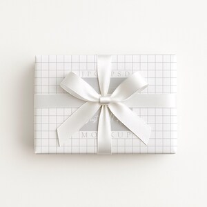 May include: A rectangular gift box wrapped in white paper with a grid pattern. A wide, light gray ribbon is wrapped around the box, tied in a bow. The background is plain white.