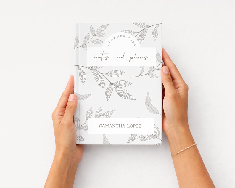 K&ouml;nnte beinhalten: Ein wei&szlig;er Planer mit floralem Design und dem Text "Planner 2020" und "notes and plans". Der Planer wird von zwei H&auml;nden gehalten. Der Name "Samantha Lopez" ist unten auf dem Planer aufgedruckt.