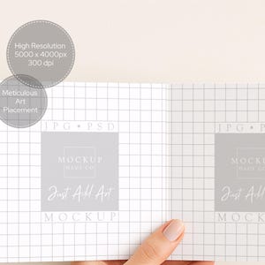 May include: A mockup image of an open book or brochure, held by a hand. The pages have a grid pattern. The text on the pages reads "MOCKUP HAUS CO" and "Just Add Art". Additional text indicates "High Resolution 5000 x 4000px 300 dpi" and "Meticulous Art Placement".