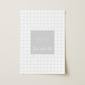 May include: A white paper with a grid pattern and the text "JPG PSD" at the top. A gray square in the center contains the text "MOCKUP HAUS CO" and "Just Add Art MOCKUP" in a handwritten style font.