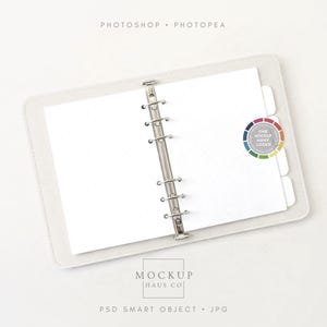 Puede incluir: Un archivador blanco abierto con páginas en blanco y divisores de pestañas. El archivador tiene un mecanismo de anillas plateado y está etiquetado con el texto "PHOTOSHOP PHOTOPEA" y "MOCKUP HAUS CO". Un círculo colorido con el texto "ONE MOCKUP MANY LOOKS" está a la derecha.