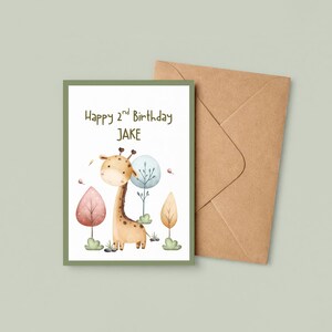 May include: A birthday card with a watercolor illustration of a giraffe and the text "Happy 2nd Birthday JAKE". The card has a green border and is accompanied by a brown envelope. The giraffe is tan with brown spots.