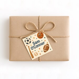May include: A brown paper-wrapped gift tied with twine and a bow. A tag featuring sports illustrations of a football, basketball, baseball bat, baseball, and a soccer ball is attached. The tag reads "Sam O'Conner".