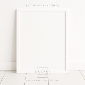 May include: A white square picture frame with a minimalist design. The frame is set against a white wall and floor, creating a clean and modern aesthetic. The text "PHOTOSHOP • PHOTOPAE" is at the top, and "MOCKUP HAUS CO" and "PSD SMART OBJECT • JPG" are at the bottom.