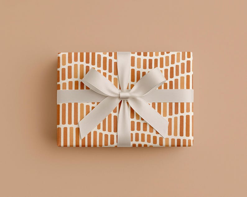 May include: A rectangular gift box wrapped in patterned paper with vertical orange and white stripes. A light gray ribbon is tied around the box with a bow on top, creating a neat and elegant presentation. The background is a solid tan color.