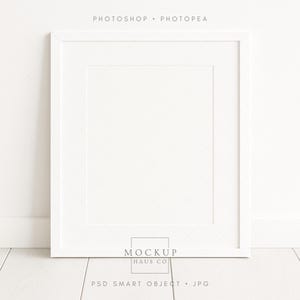 Può includere: Una cornice quadrata bianca con un passe-partout bianco, appoggiata a una parete bianca. La cornice è su un pavimento di legno bianco. Il testo "PHOTOSHOP • PHOTOPEA" è in alto. Il testo "MOCKUP HAUS CO" e "PSD SMART OBJECT • JPG" sono in basso.