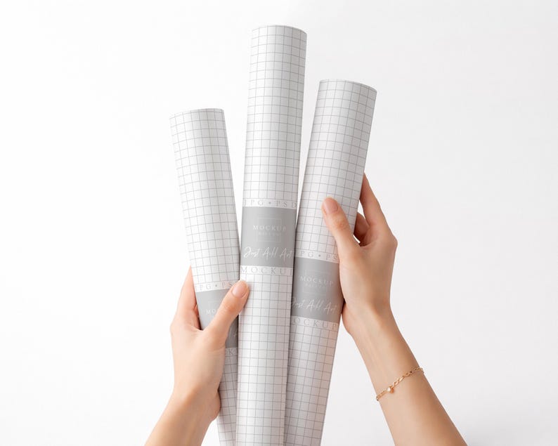 May include: Three rolls of white grid paper are held by hands against a white background. Each roll is wrapped with a gray band that has text on it. The grid paper is a light gray color.