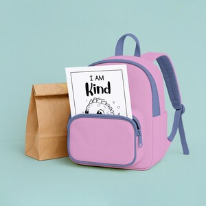 May include: A pink backpack with blue accents and a front pocket holds a coloring page that reads "I AM Kind." A brown paper lunch bag sits to the left of the backpack. The background is a light teal color.