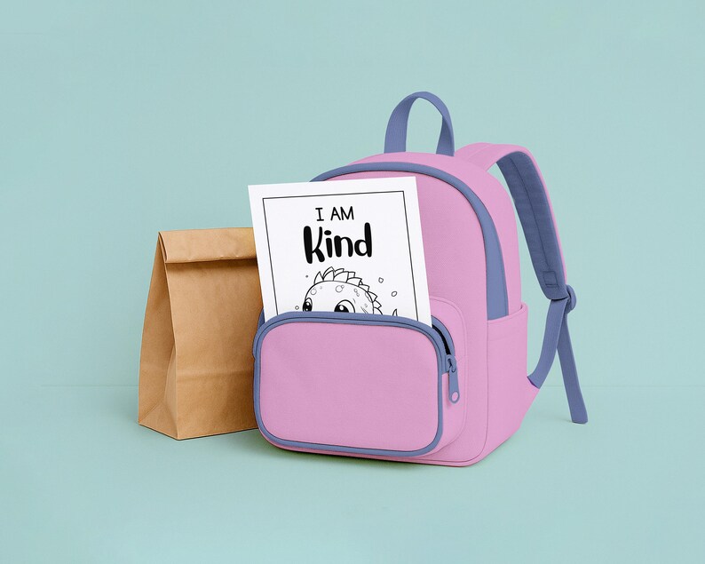 May include: A pink backpack with blue accents and a front pocket holds a coloring page that reads "I AM Kind." A brown paper lunch bag sits to the left of the backpack. The background is a light teal color.
