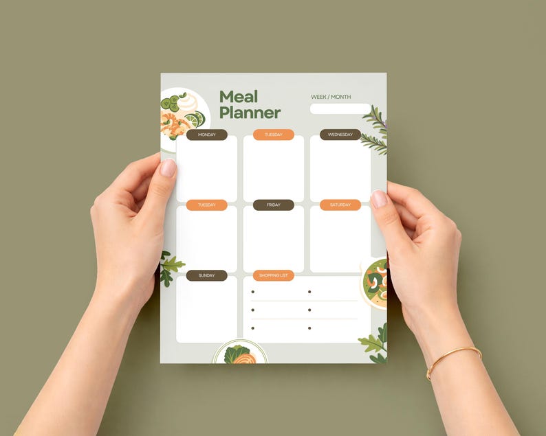 Puede incluir: Un planificador de comidas con las palabras "Meal Planner" en la parte superior. El planificador tiene secciones para cada d&iacute;a de la semana, con una secci&oacute;n de lista de compras en la parte inferior. El planificador est&aacute; sostenido por dos manos contra un fondo verde.