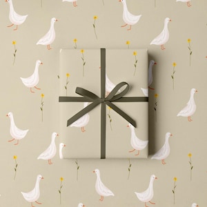 May include: A wrapped gift with a dark green ribbon on a background of light beige wrapping paper. The paper is patterned with white geese and yellow flowers. The gift wrap has the same pattern as the background.