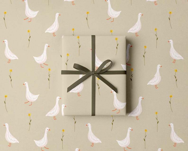 May include: A wrapped gift with a dark green ribbon on a background of light beige wrapping paper. The paper is patterned with white geese and yellow flowers. The gift wrap has the same pattern as the background.