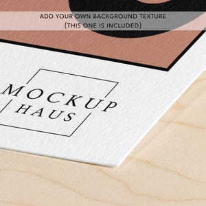 May include: A white paper mockup featuring the black text MOCKUP HAUS enclosed in a thin black square outline. Above this, a semi-transparent horizontal bar contains the black text ADD YOUR OWN BACKGROUND TEXTURE (THIS ONE IS INCLUDED).
