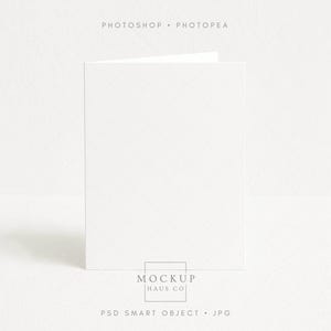 May include: A blank, folded greeting card in a vertical orientation, set against a soft, textured white background. The card is slightly open, revealing the inside. The top of the image reads "PHOTOSHOP • PHOTOPEA". The bottom of the image reads "MOCKUP HAUS CO" and "PSD SMART OBJECT • JPG".