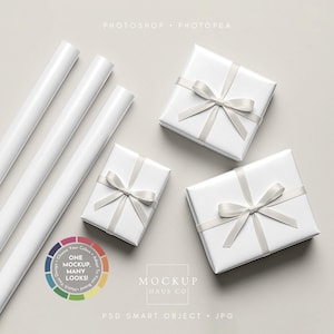 Puede incluir: Cajas de regalo blancas atadas con lazos de cinta plateada, junto a rollos de papel de regalo blanco. La imagen incluye texto que dice "ONE MOCKUP, MANY LOOKS!" y "MOCKUP HAUS CO."
