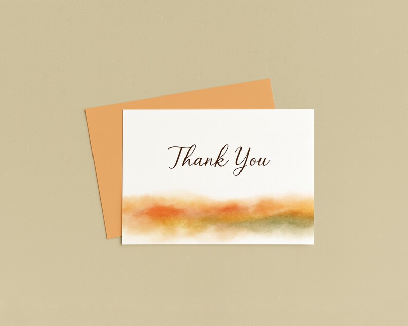 K&ouml;nnte beinhalten: Eine wei&szlig;e Karte mit dem Schriftzug "Thank You" in eleganter Schrift, &uuml;ber einer Aquarelllandschaft in Orange-, Gelb- und Gr&uuml;nt&ouml;nen. Ein orangefarbener Umschlag liegt hinter der Karte, vor einem neutralen Hintergrund.