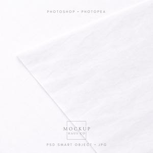 May include: A white fabric mockup with a textured surface. The corner of the fabric is folded over, creating a diagonal line across the image. The text "PHOTOSHOP • PHOTOPAE" is at the top, and "MOCKUP HAUS CO" and "PSD SMART OBJECT • JPG" are at the bottom.