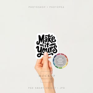 May include: A hand holding a white sticker with the phrase "Make it yours" in black script. A color wheel with the text "One Mockup Many Looks" is next to the sticker. The background is plain white.
