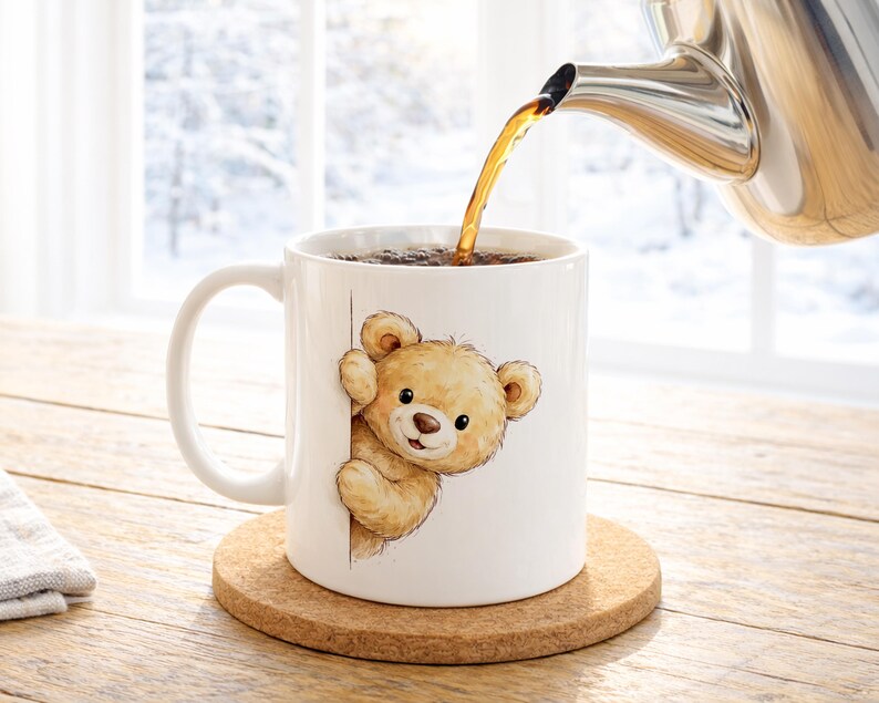 May include: A white ceramic mug featuring a cartoon teddy bear design, with a brown cork coaster underneath. Hot liquid is being poured from a stainless steel teapot into the mug. The background shows a snowy winter scene.