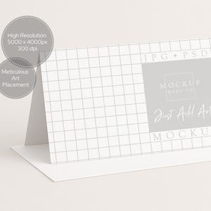 Pu&ograve; includere: Un mockup di biglietto bianco piegato con un motivo a griglia sul davanti. La carta presenta il testo "MOCKUP HAUS CO" e "Just Add Art". Il testo aggiuntivo include "High Resolution" e "Meticulous Art Placement".