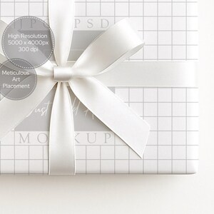 May include: A white gift box wrapped in grid-patterned paper and tied with a white satin ribbon and bow. The image includes text that reads "High Resolution 5000 x 4000px 300 dpi" and "Meticulous Art Placement". The word "MOCKUP" is also visible.