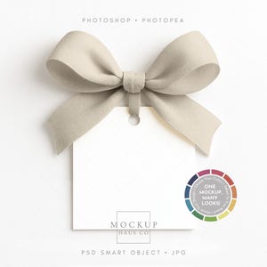 May include: A blank white tag with a beige bow tied at the top. The tag has a small hole at the top for attaching to a product. The text "MOCKUP HAUS CO" is printed at the bottom of the tag. A color wheel is in the bottom right corner.