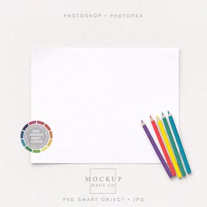 May include: A white rectangular paper with a subtle grid pattern, alongside five coloured pencils in purple, red, yellow, green, and teal. A circular colour palette and text reading "Mockup Haus Co" are also present.
