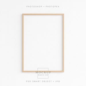 Puede incluir: Un marco de fotos rectangular de madera clara, vacío, sobre un fondo blanco. El marco tiene un diseño sencillo y limpio. Las palabras "PHOTOSHOP • PHOTOPEA" están en la parte superior. Las palabras "MOCKUP HAUS CO" están en la parte inferior, junto con "PSD SMART OBJECT • JPG".