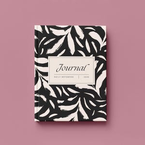 May include: A hardcover journal with a black and white abstract leaf pattern. The journal cover features the word "Journal" in an elegant font, with "DAILY NOTEBOOK | 2020" below. The journal is set against a pink background.