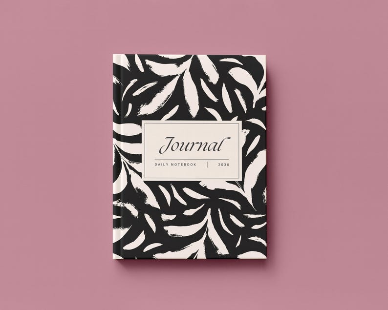 May include: A hardcover journal with a black and white abstract leaf pattern. The journal cover features the word "Journal" in an elegant font, with "DAILY NOTEBOOK | 2020" below. The journal is set against a pink background.