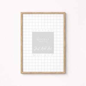 May include: A rectangular wooden picture frame with a grid pattern background. The frame has a light brown color and contains the text "JPG PSD", "MOCKUP HAUS CO", and "Just Add Art MOCKUP" in a light gray color.
