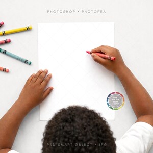 May include: A child's hands are shown drawing with a red crayon on a blank white paper. Several colorful crayons are scattered around the paper. The image is a mockup for art or design.