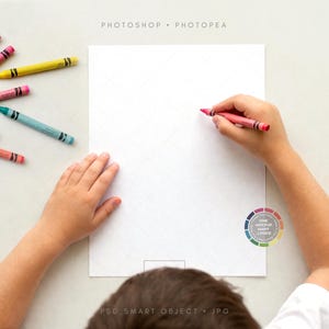 May include: A child's hands hold a red crayon over a blank white sheet of paper. Various crayons in red, orange, pink, green, yellow, and blue are scattered on the white surface. The image includes the text "PHOTOSHOP • PHOTOPEA" and "PSD SMART OBJECT • JPG".