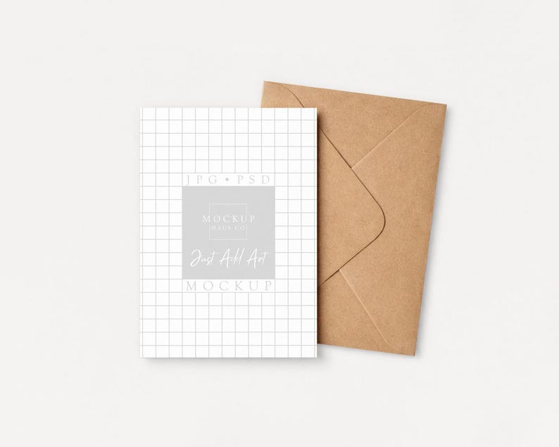 May include: A white card with a grid pattern and text that reads "Just All Art Mockup" is next to a brown envelope. The card has a light gray square with the text "Mockup Pays Co." The background is a solid off-white color.