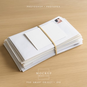 May include: A stack of white envelopes and a blank card, secured with a tan rubber band. The top envelope features a U.S. flag postage stamp. The items rest on a light brown wooden surface. The words "Photoshop Photopae" are at the top.
