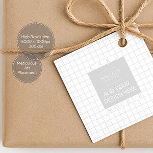 May include: A brown paper-wrapped parcel tied with twine, featuring a white tag with a grid pattern. The tag displays the words "CARD", "ADD YOUR DESIGN HERE", and "MOCKUP". The package also has text that reads "High Resolution 5000 x 4000px 300 dpi" and "Meticulous Art Placement".